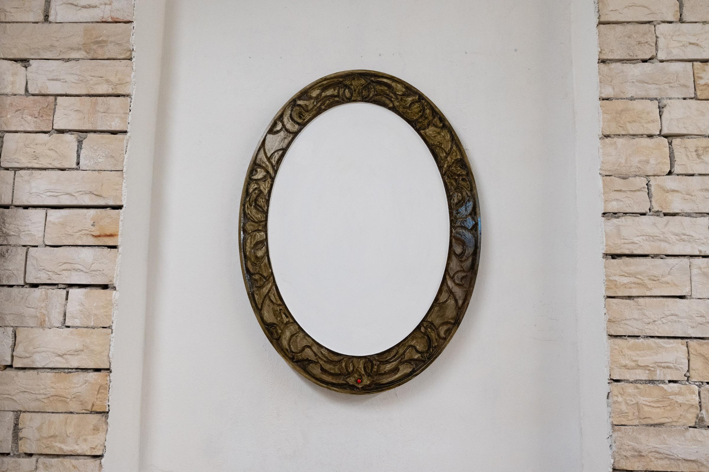A large oblong frame sits in the center of a white wall with an ornate brown outline and white painted center.