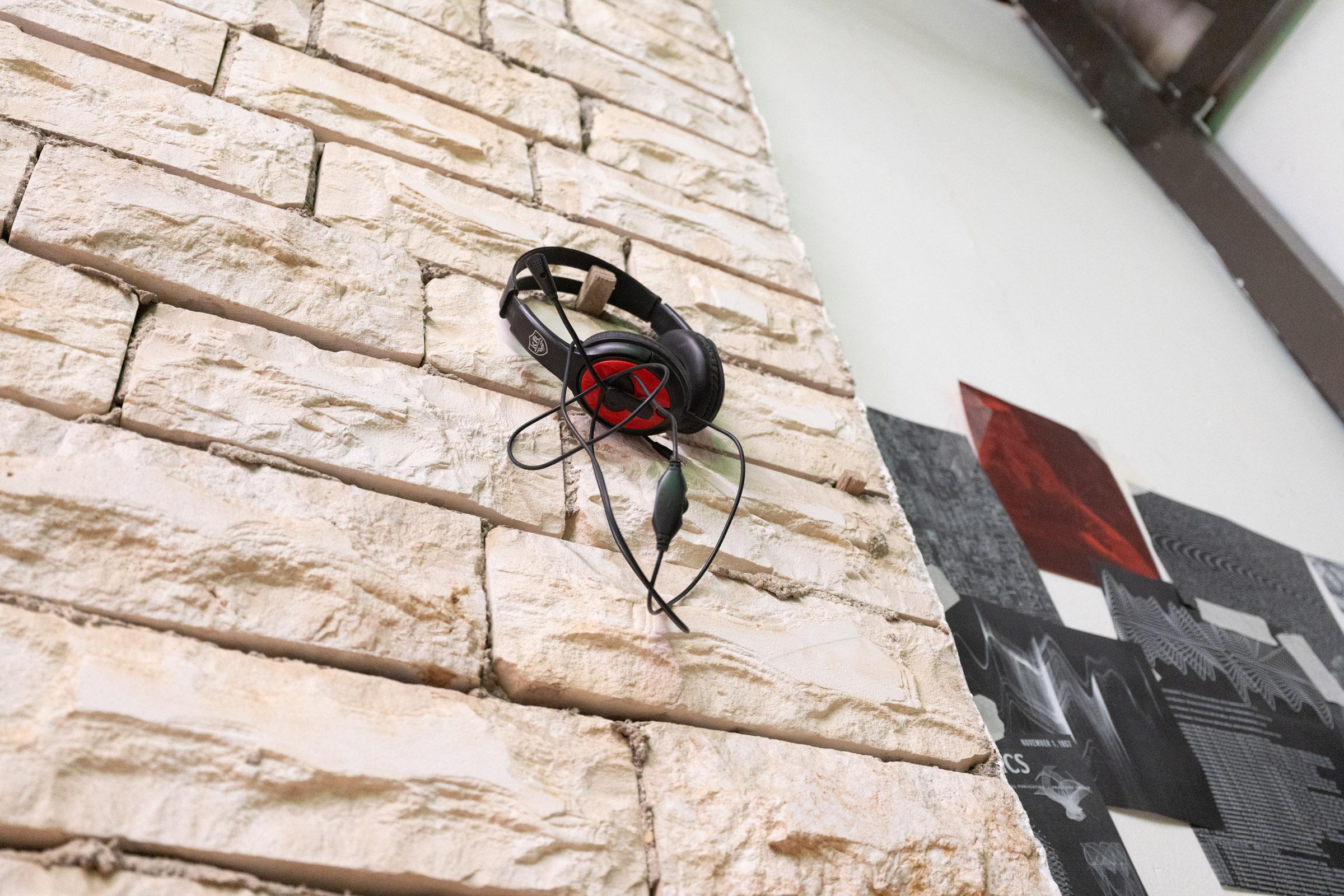Light, sandy brick wall with a pair of wired headphones on a hook.