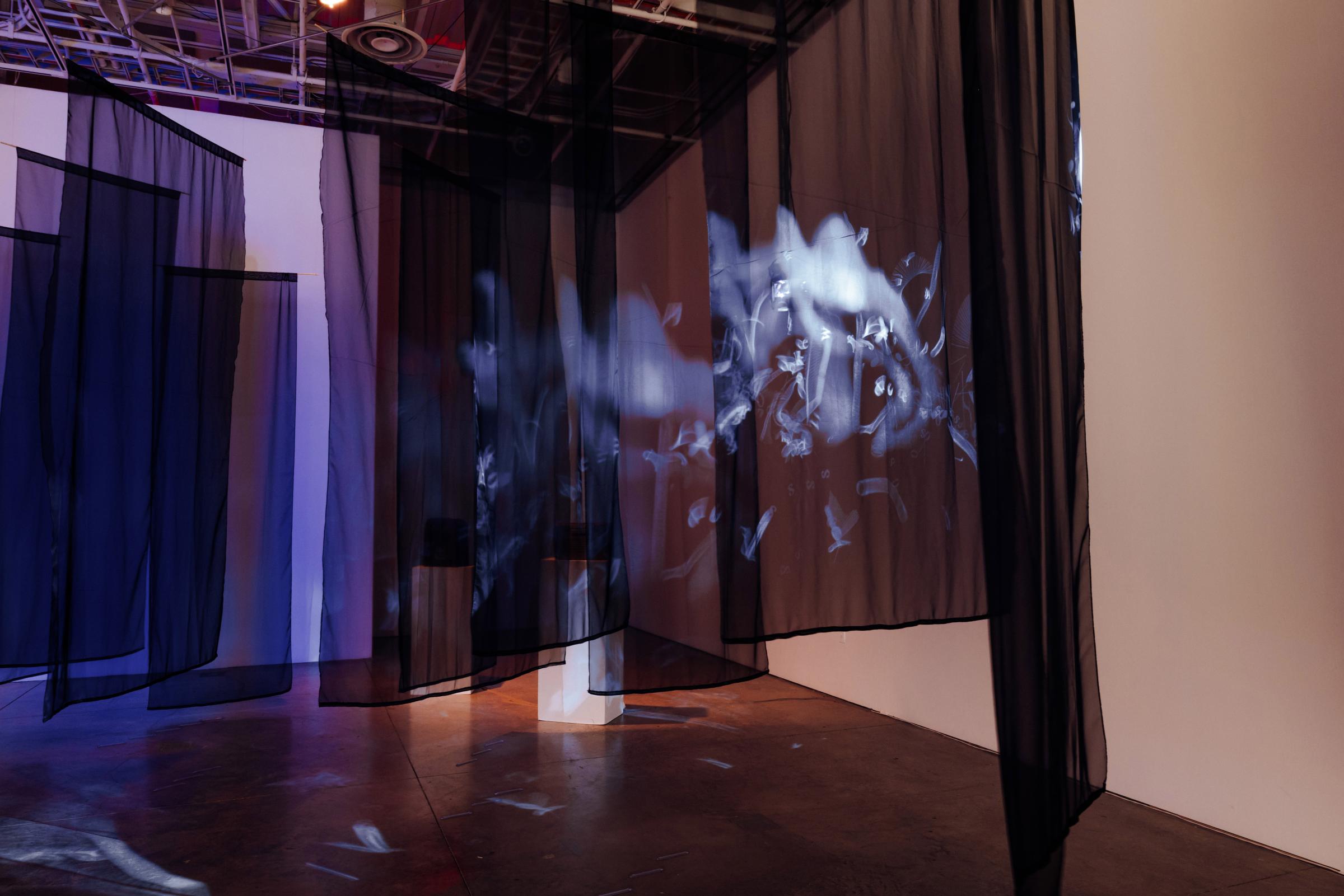 Projected in white onto translucent black fabric, letters flow into a smoke like array. 
