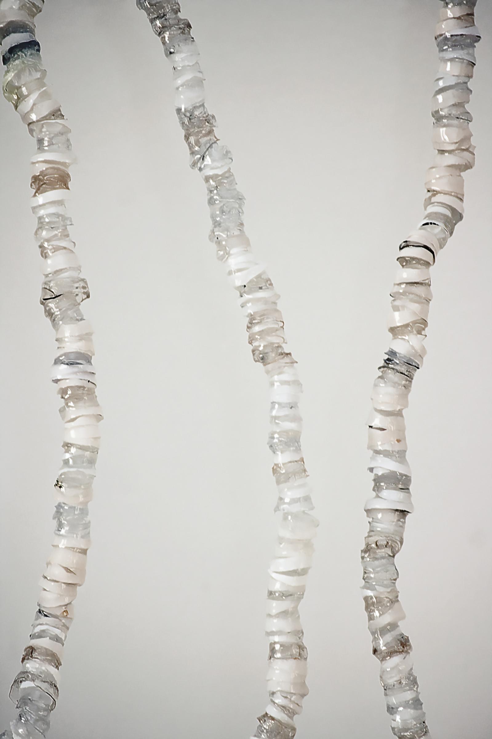  A close-up of a sculpture presenting three curved columns resembling spines, composed of translucent, grey, and white segments against a light grey background, intentionally designed to break and be repaired daily.