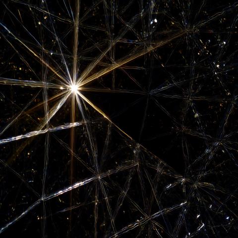 A net of crystalline threads refracting line against a black background. In the upper left an intersection glows brightly, and to its lower right the threads open to a section of solid darkness.