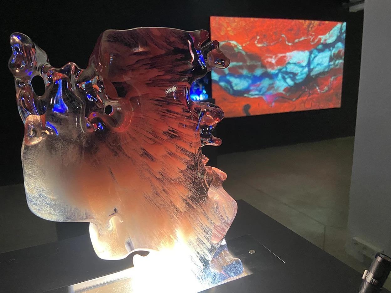 Glass sculpture reflecting light, with a red and blue projection on the wall behind.