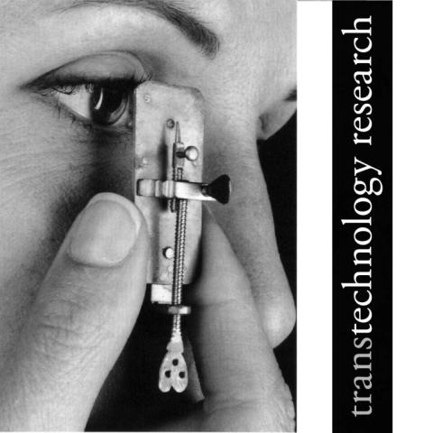 A person is holding a small mechanical device close to their eye with the text "transtechnology research" displayed vertically beside them.
