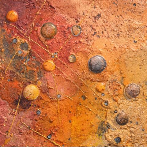 An abstract textured surface in warm tones of orange, gold, and red, resembling a cosmic or geological landscape. The composition glows with energy, evoking motion, connection, and transformation.
