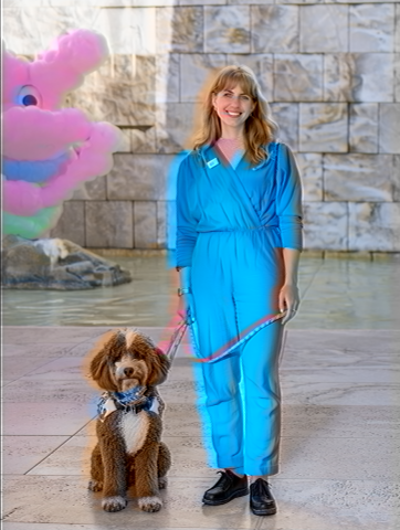 An uncanny AI rendering of a red and white poodle mix resembling Bob Ross, Zsofi’s service dog, and Zsofi, a white thirtysomething woman with wavy blond hair and bangs, standing in a teal jumpsuit with a pink leash attached to Bob. The colors and forms in the image are dreamy and glitching, as if on an old VHS tape. Zsofi and Bob are posing in front of a beige travertine stone fountain, with water flowing from a clownish, bubblegum pink cyclops monster that Midjourney hallucinated.