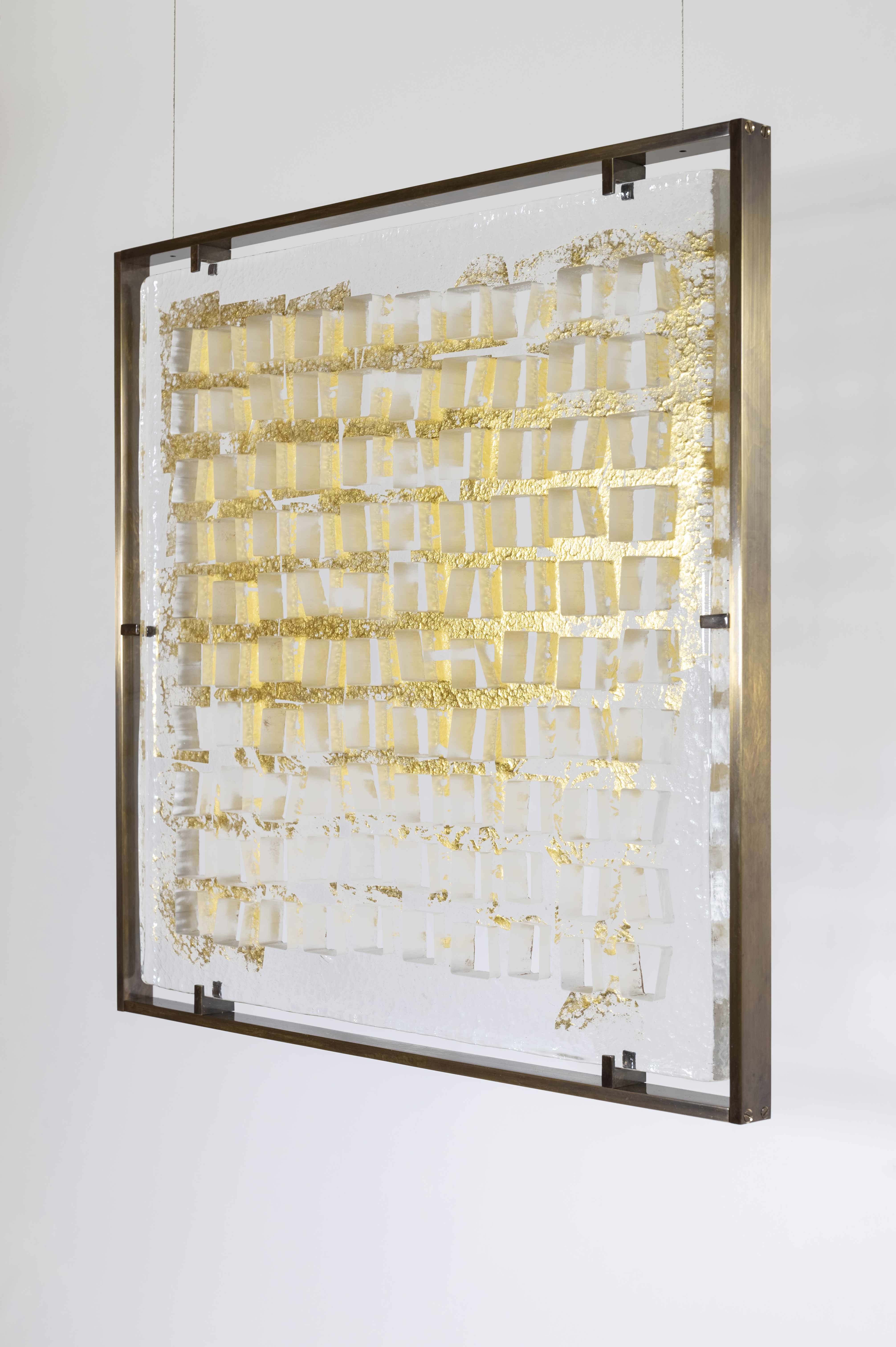Rectangular glass hanging from two wires that include gold leaf square pattern of artist Vera Molnars computational pattern.