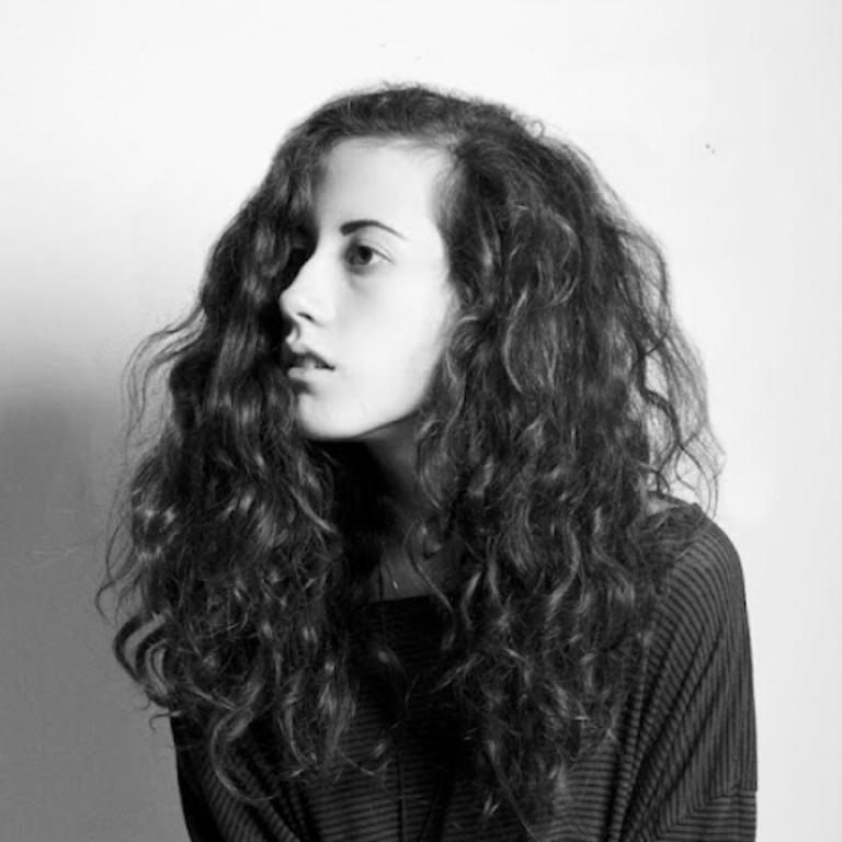 Meesh in black and white with a white background. They are looking to the side, wearing a striped long sleeve shirt, and have big curly hair.