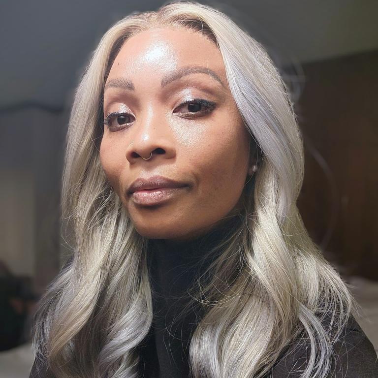 Image of medium brown skinned person with black turtleneck and long platinum/ash hair.