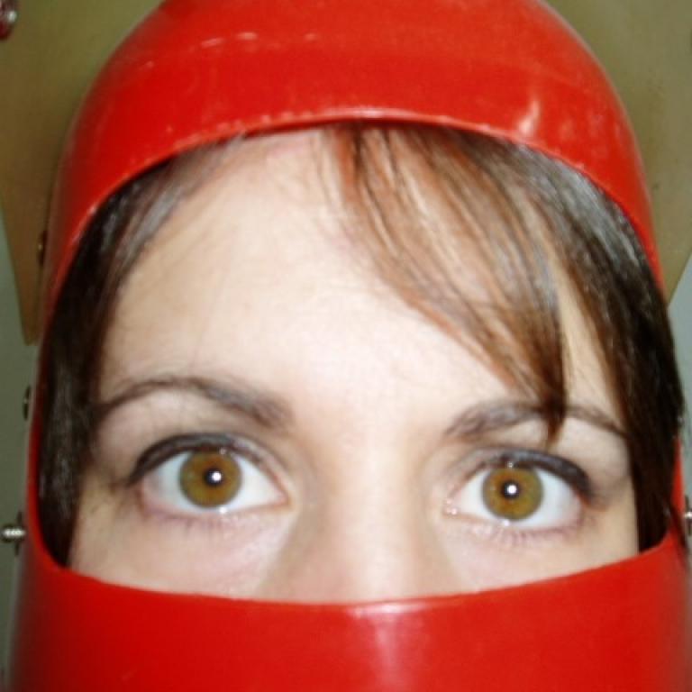 a closeup of a woman wearing a red helmet.  She has brown hair and hazel eyes.