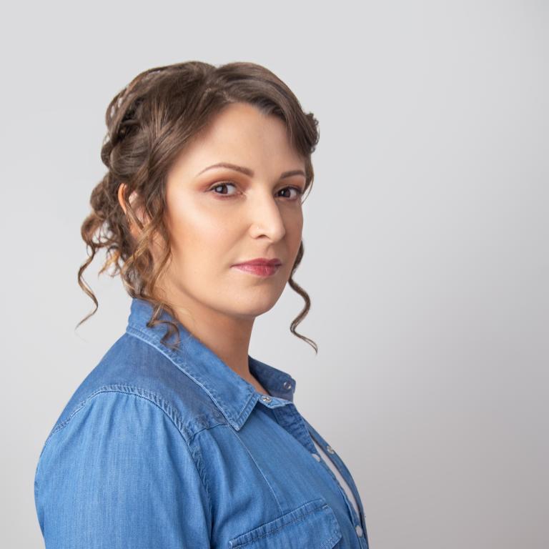 Michelle L Herman has brown curly hair and is pictured wearing a blue chambray shirt